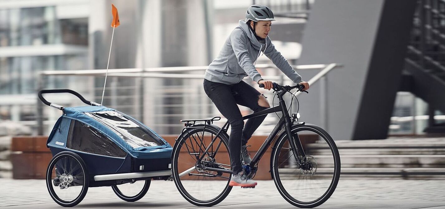 Eine Frau fährt auf einem Fahrrad mit einem Kinderanhänger.